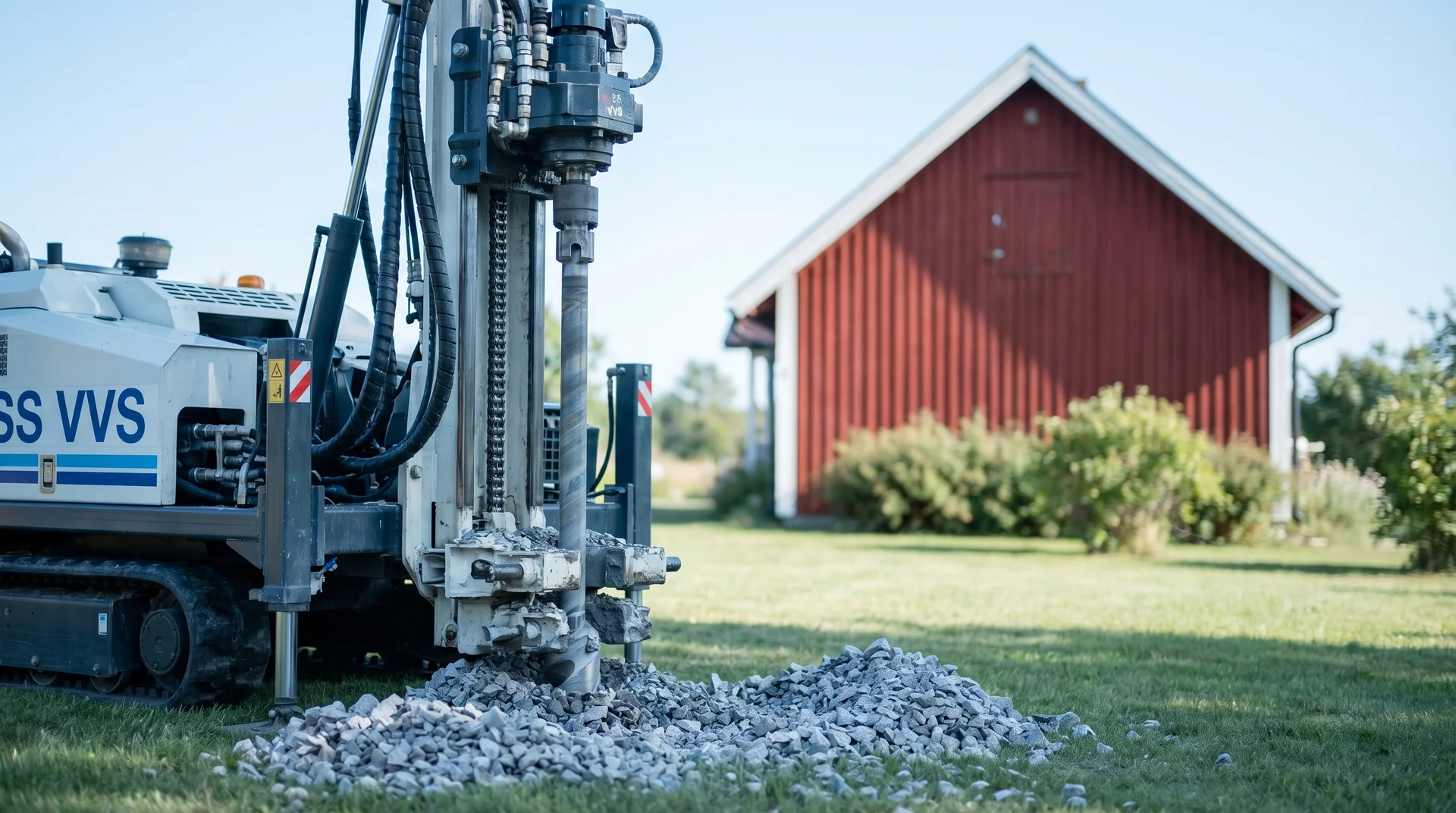 Borrmaskin borrar i mark framför röd lada på gräsmatta.